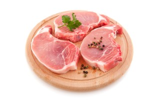Raw pork chops with garnish on a circular wood cutting board - jbs usa - pork settlement -pork class action