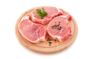 Raw pork chops with garnish on a circular wood cutting board - jbs usa