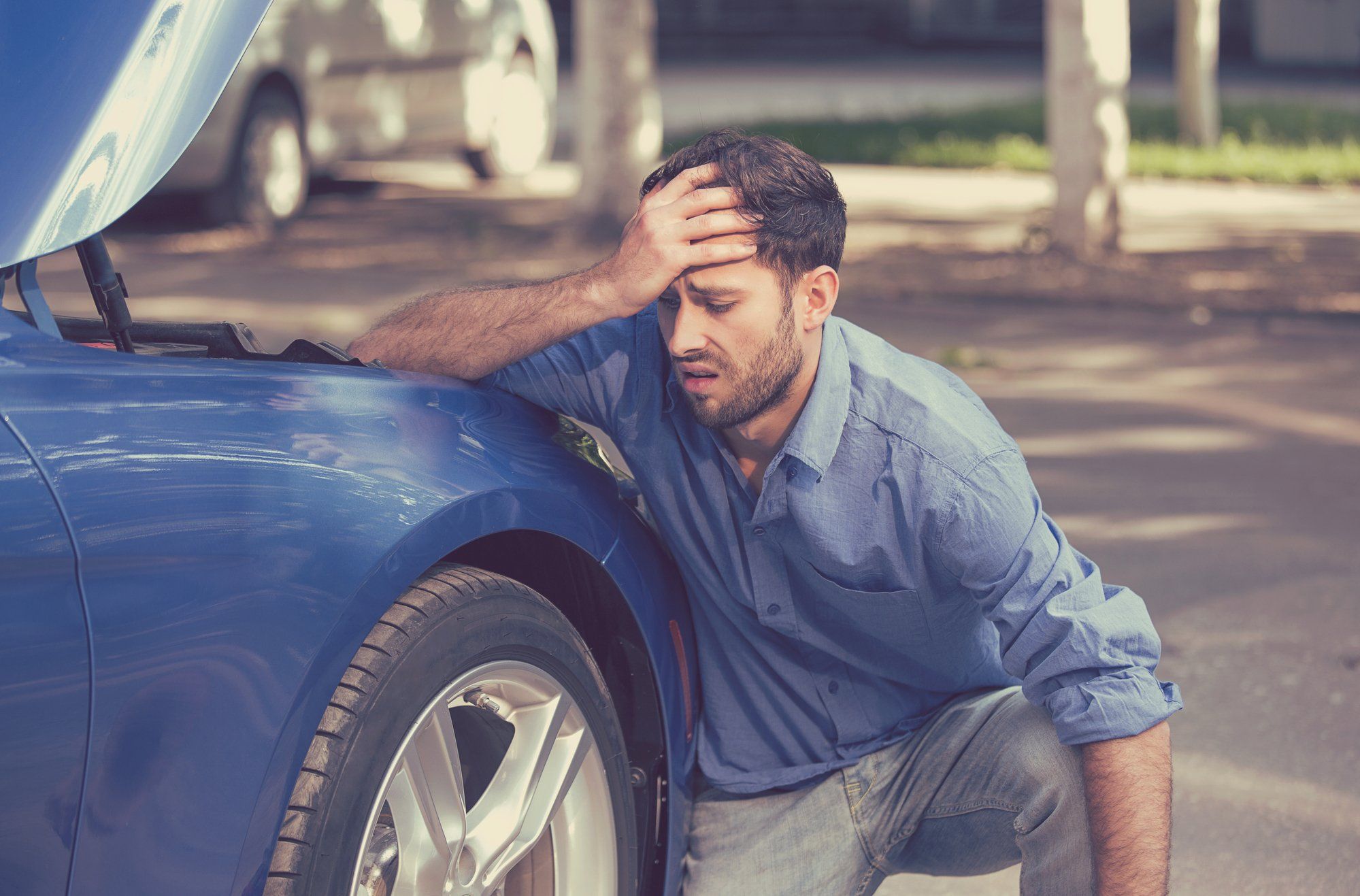 stressed man squatting next to broken down car
