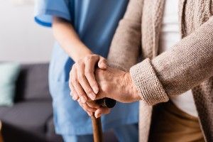 A nurse helps an elderly woman with a cane - Nursing home deaths
