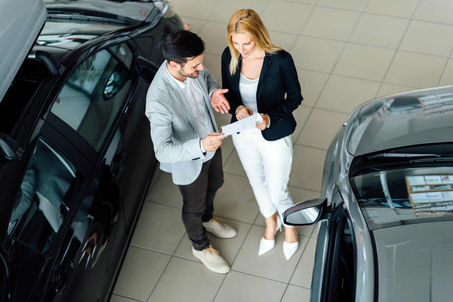 A salesperson and a customer talk over a paper while standing in a car dealership showroom - reynolds