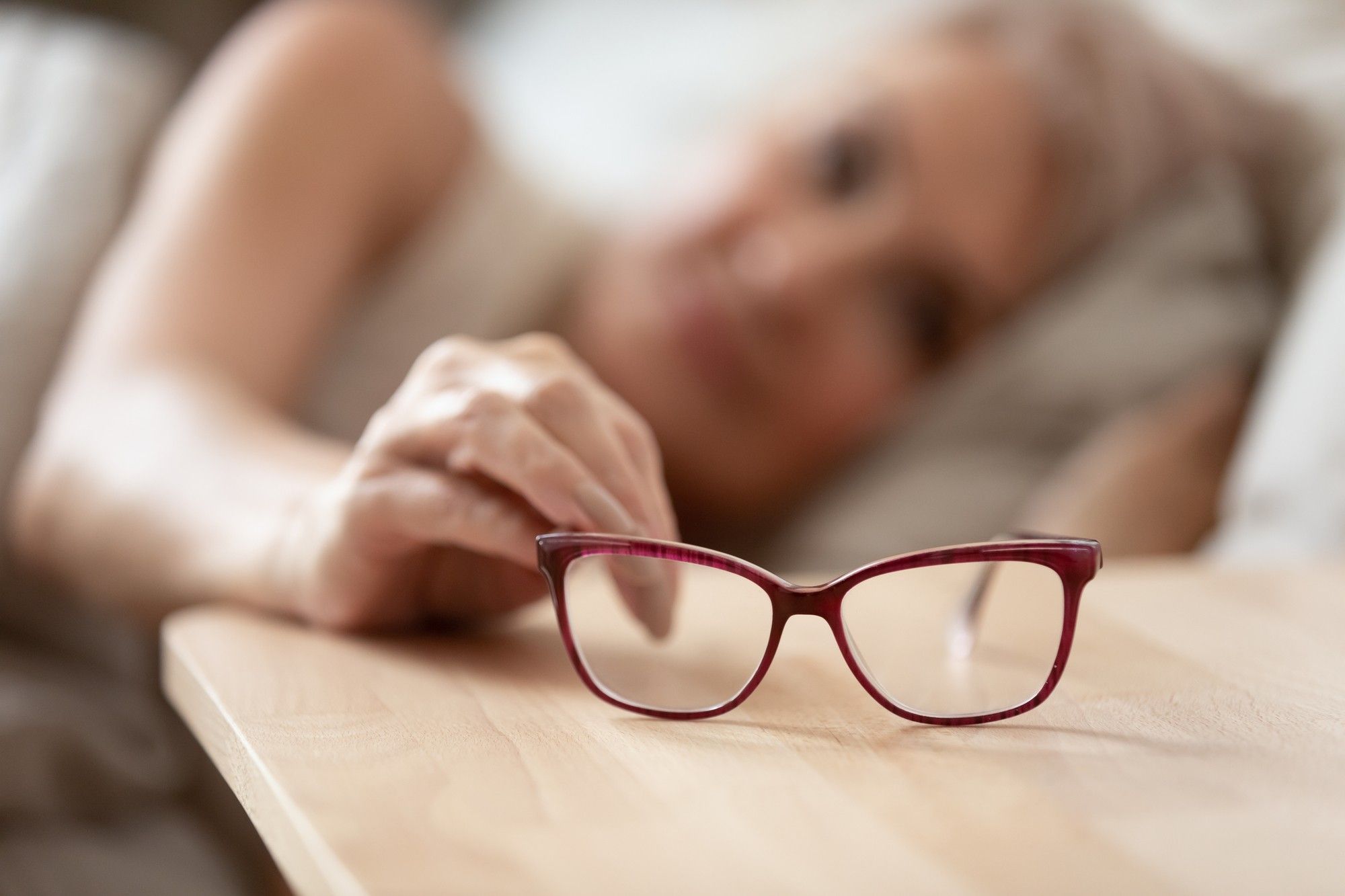 older woman in bed reaching for glasses