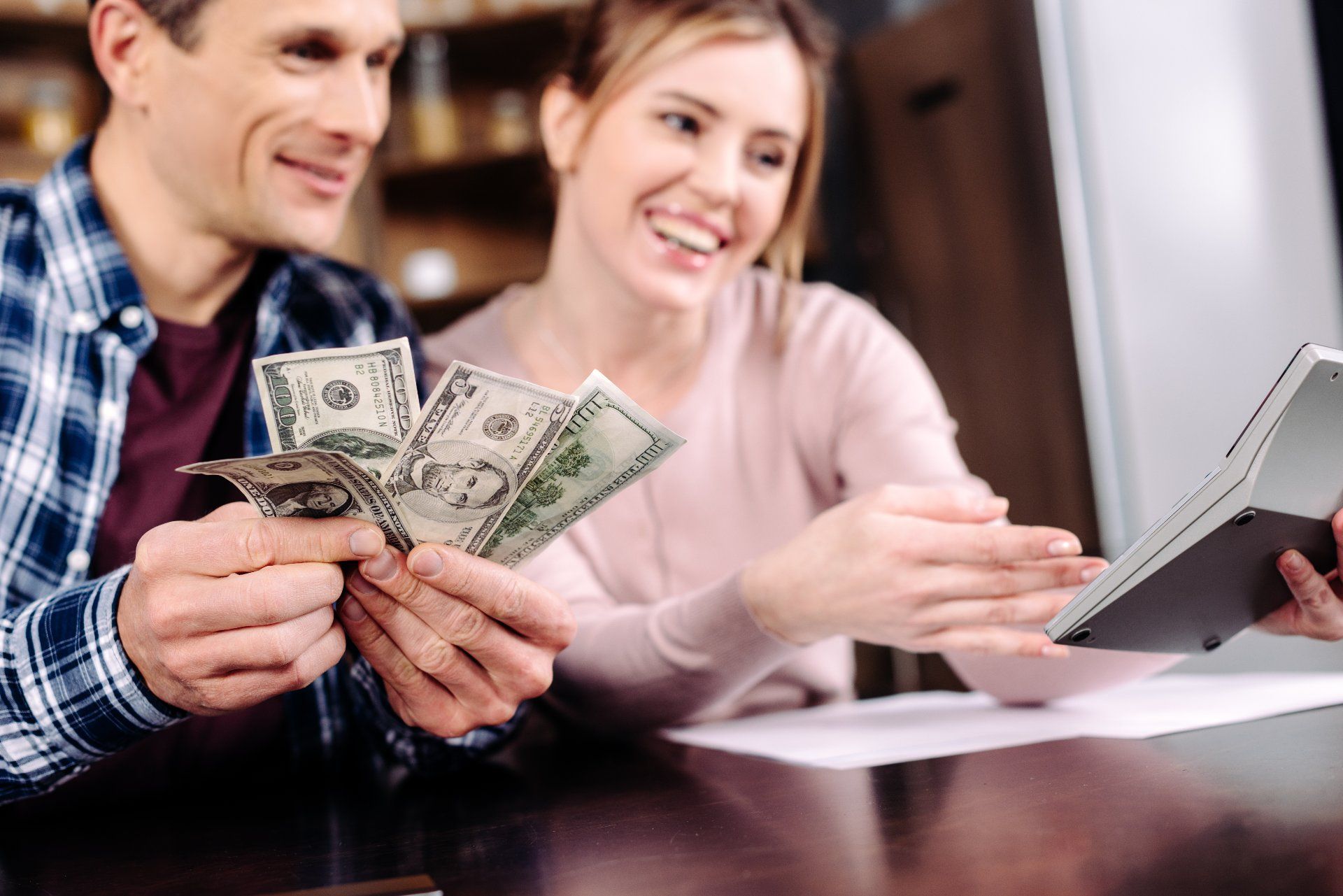 A happy couple at a table holds fanned out cash while looking at a calculator - ftc refunds