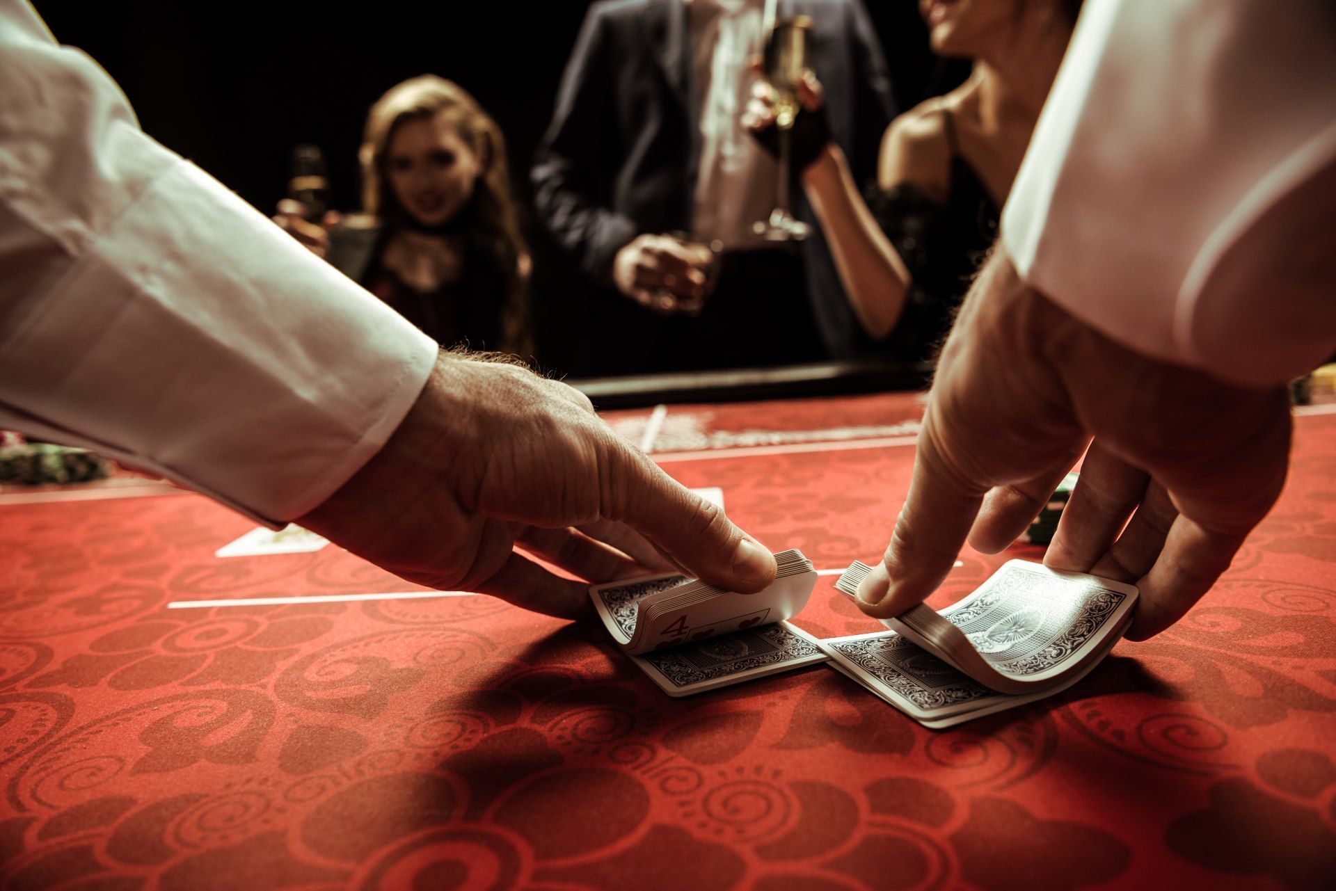 Closeup of a dealer in a casino shuffling cards at a game table as people stand nearby - Wind Creek Casino