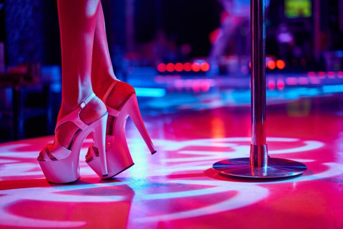 A dancer's feet in heels are shown near a pole at a gentlemen's club