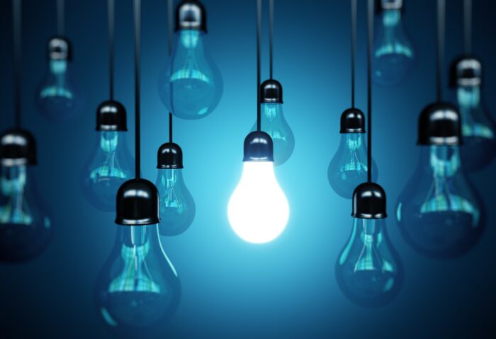 Light bulbs hang from the ceiling, with one illuminated, against a blue background - electricity