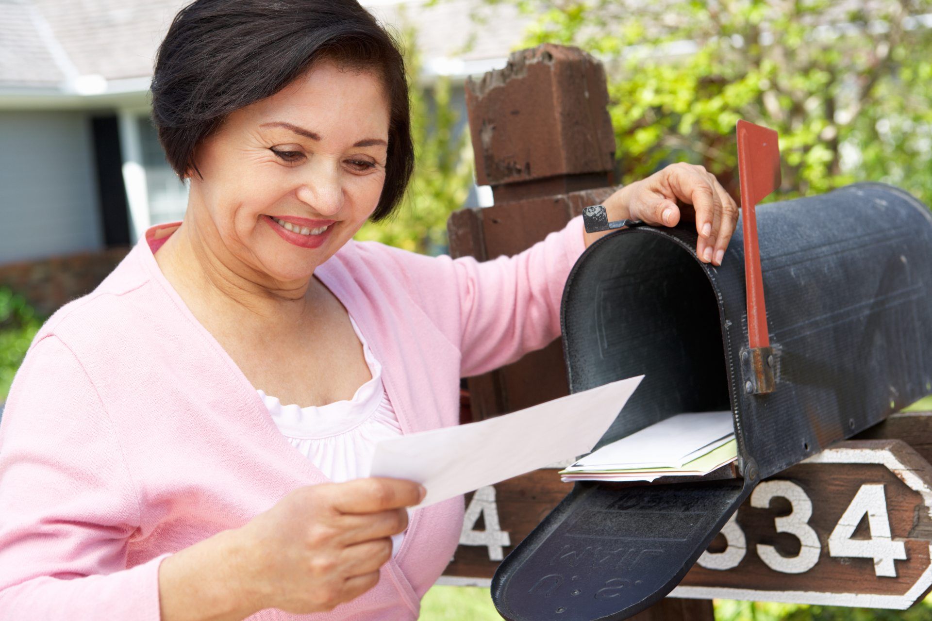 Happy woman smiles at a letter in her hand as she stands near an open mailbox - ftc refunds - student loan debt