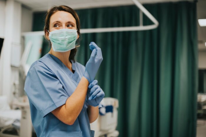 A female nurse in scrubs and a surgical mask puts on a blue glove - CHI Franciscan settlement