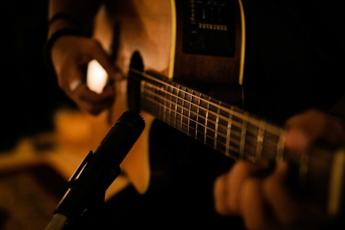 Hands play an acoustic guitar near a microphone - Performers Royalties - royalties class action settlement