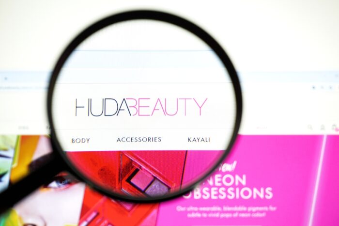 Huda Beauty logo is seen on a computer screen under a magnifying glass - Huda eyeshadow