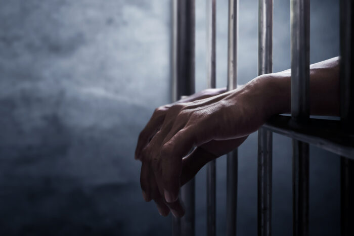 A pair of hands reaching through jail cell bars.