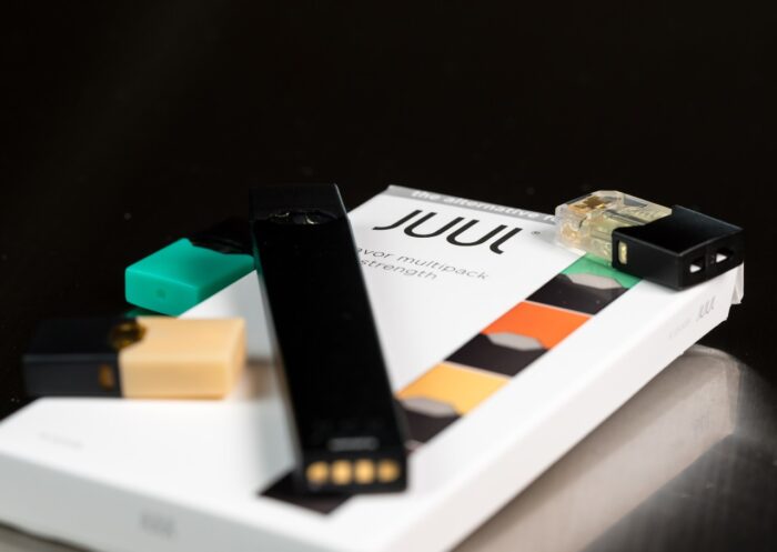 Juul e-cigarette or nicotine vapor dispenser box and JUULpod on dark background
