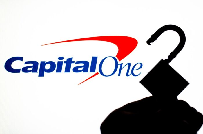 Capital One Bank logo on the screen in a main focus and a blurred silhouette of the open lock. Conceptual photo for news about the bank data breach.