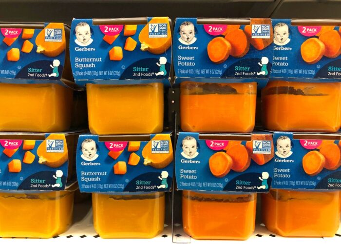 Plastic containers of Gerber's brand 2nd stage baby foods on a grocery store shelf, Butternut Squash and Sweet Potato flavors.