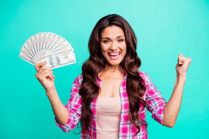 happy beautiful woman with money in hand wearing casual plaid checkered pink shirt outfit isolated teal bright vivid background