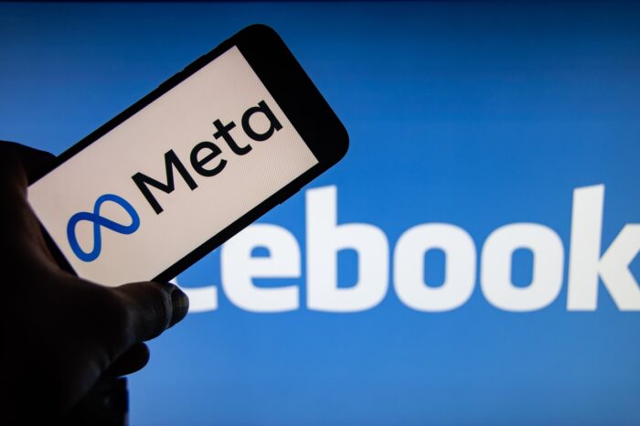 The brand logo "Meta" on the display of a smartphone in front of the Facebook logo.
