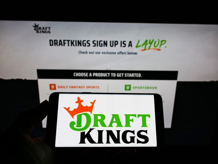 Person holding smartphone with logo of US sports betting company DraftKings Inc. on screen 