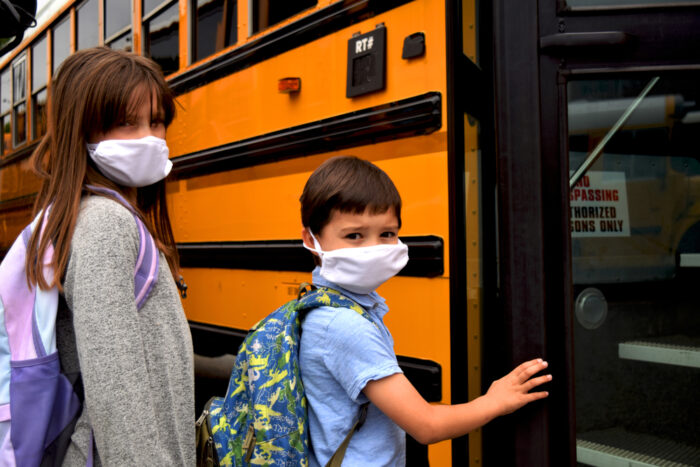 Two children board a school bus while wearing face masks.