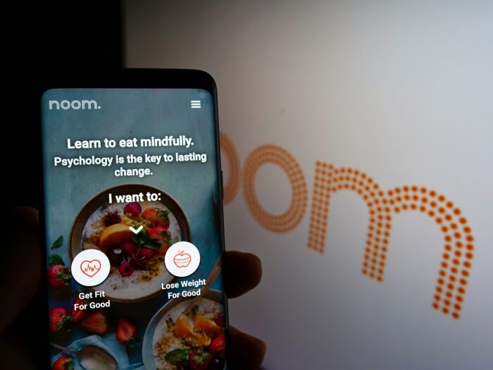 Person holding mobile phone with website of US weight-loss platform company Noom Inc. on screen in front of logo.