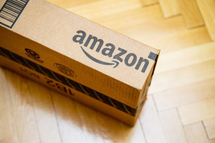 Amazon logotype printed on cardboard box side seen from above on a wooden parquet floor.