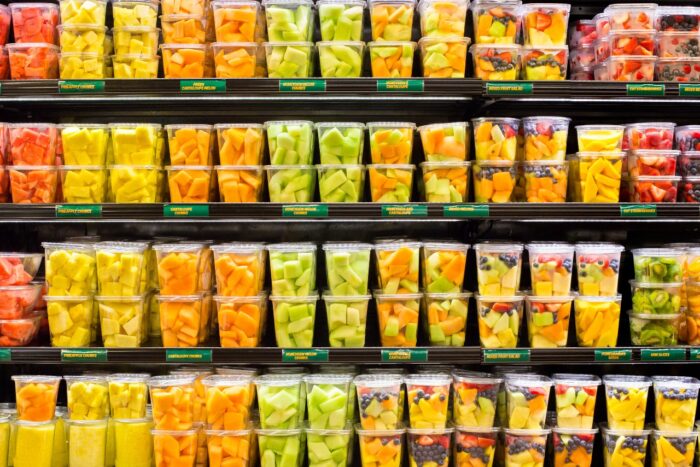 supermarket grocery display case with fresh cut fruit on shelves in plastic containers