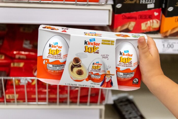 child's hand holding a package of kinder joy brand sweet cream topped with cocoa wafer bites.