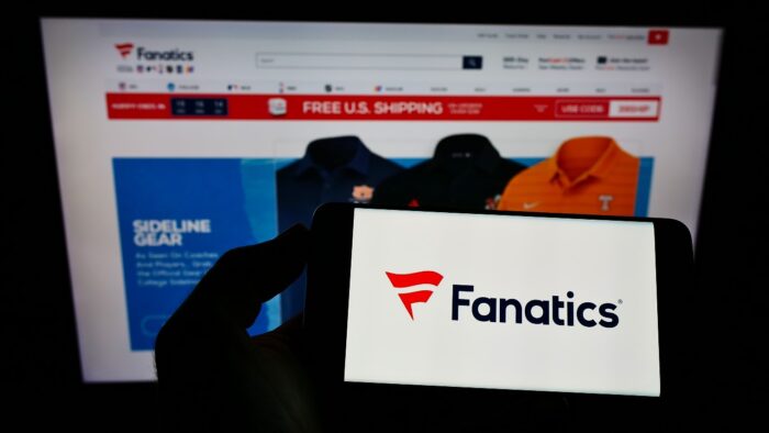 Person holding smartphone with logo of US online sportswear retailer Fanatics Inc. on screen in front of website.