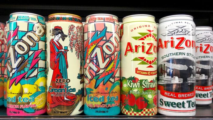 Grocery store shelf with 23 ounce cans of Arizona brand ice teas in various flavors.