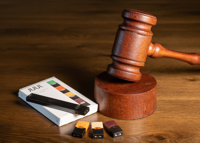 Juul e-cigarette or nicotine vapor dispenser box with Judge's gavel for lawsuit.
