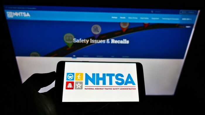 Person holding smartphone with logo of National Highway Traffic Safety Administration (NHTSA) on screen in front of website.