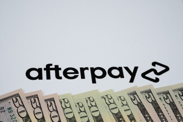 Dollar bills and blurrred Afterpay company logo seen paper background.