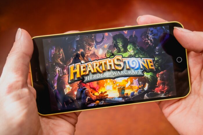 Hands holding a smartphone with Hearthstone intro on display screen. Activision Blizzard class action, Hearthstone, cards