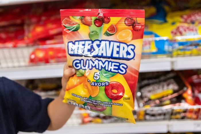 Child's hand holding a bag of Lifesavers brand gunnies candy in a supermarket aisle.