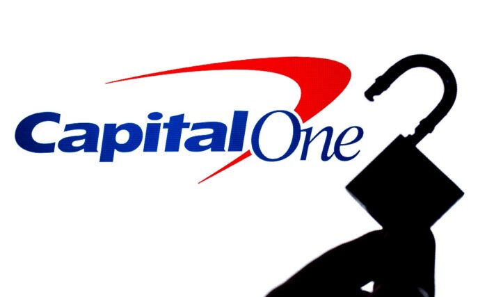 Capital One Bank logo on the screen in a main focus and a blurred silhouette of the opened lock - capital one data breach settlement - Capital One customer data security litigation