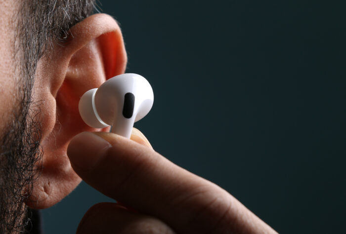 Close of man's ear showing his fingertips placing an Apple AirPod into his ear.