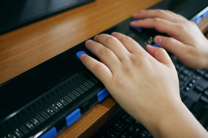Close-up blind person hands using computer with braille display or braille terminal a technology assistive device for persons with visual disabilities.