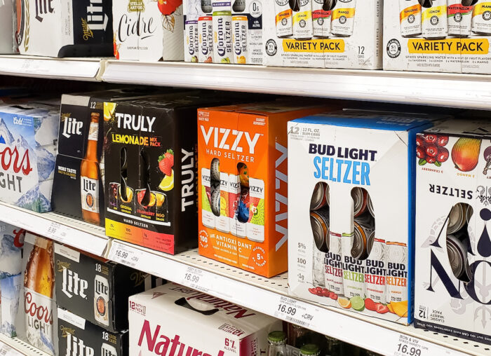 A view of several shelves filled with a variety of popular brands of hard seltzer beverages, on display at a local grocery store.