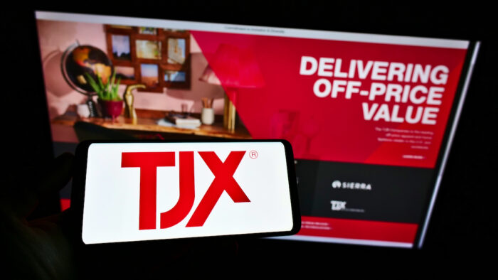 Person holding smartphone with logo of US department store company The TJX Companies Inc. on screen in front of website.