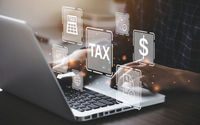 A person uses a laptop with tax, money, and caluculator graphics floating above the keyboard - ftb llc fees - california franchise tax board