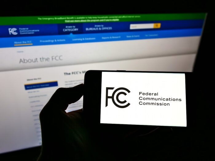 Person holding smartphone with seal of US agency Federal Communications Commission (FCC) on screen in front of website.