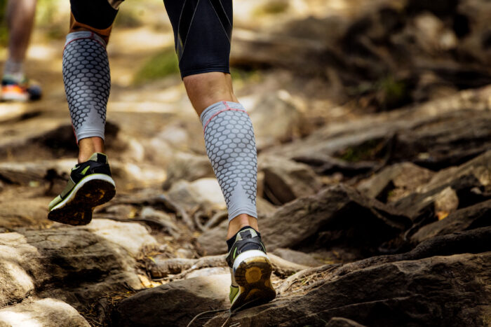 Marathon runner running rocks in mountain. Closeup of legs compression socks and shoes.