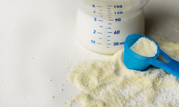 Powder milk for baby and blue spoon on light background close-up.
