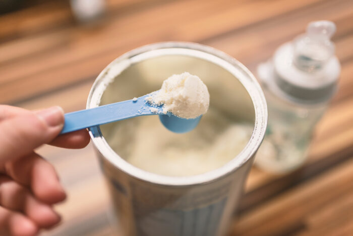 Powder milk and blue spoon on light background close-up.