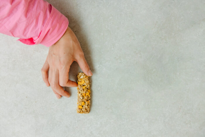 A person in a long-sleeve pink shirt holds a granola bar against a grey background - general mills - nature valley class action