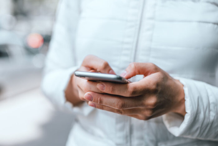 Close up of woman's hands in white jacket holding grey smartphone and typing a message with both hands on street - madison reed class action
