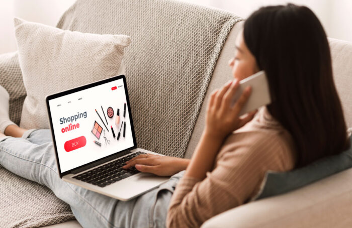 Back view of woman browsing online make up store, talking on phone, sitting at home.