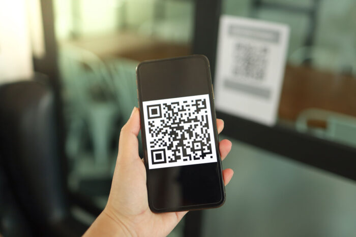 Close up of a hand holding a smartphone which is displaying a large QR code - American Apparel & Footwear Association - clothing labels