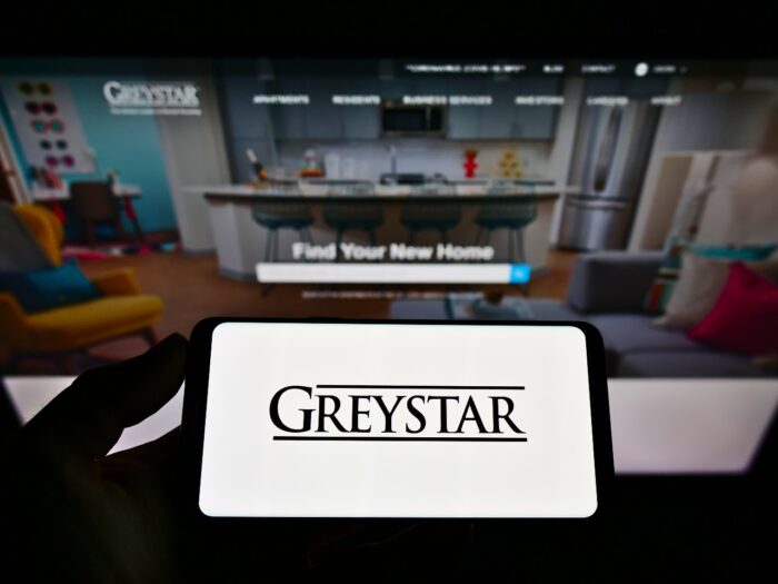Person holding mobile phone with logo of Real estate company Greystar Real Estate Partners LLC on screen in front of website - greystar class action lawsuit