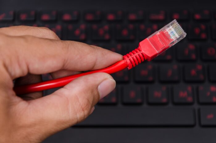 Red LAN Internet cable in man hand on black laptop computer with red back-light keyboard background - RCN late fee settlement, RCN class action