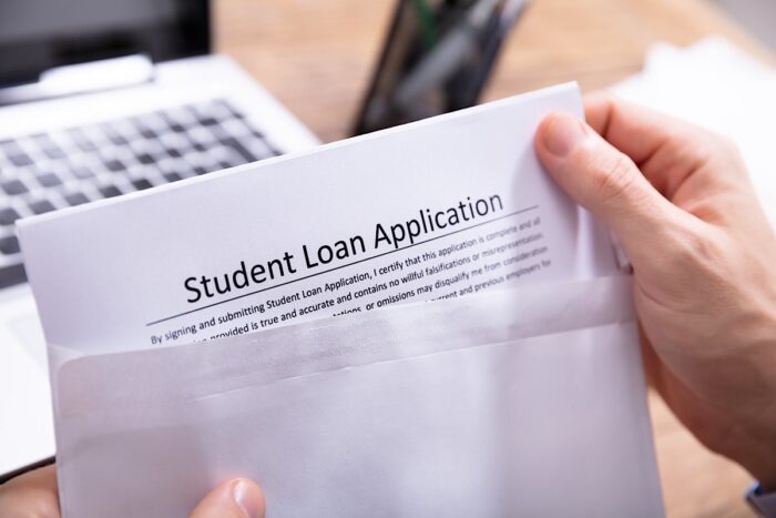 Close-up Of A Person's Hand Removing Student Loan Application Form From White Envelope.